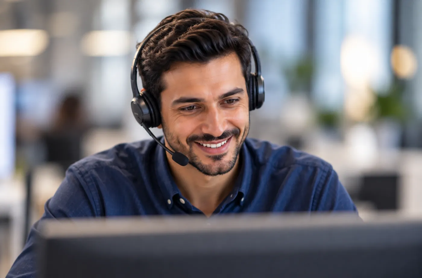A smiling support team member wearing a headset, working at his computer